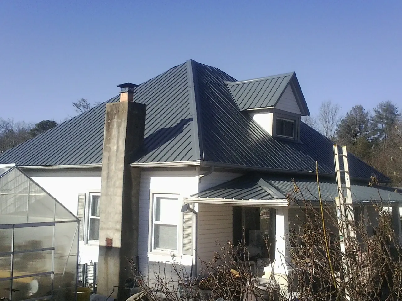 Dark blue standing seam metal roof on a white farmhouse with dormer — Slate & Tile Roof Repair by Roofing Brothers in Lake Dallas