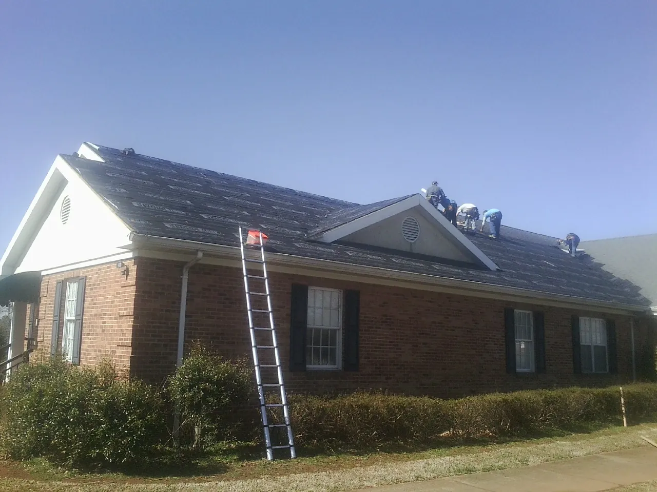 Crew tearing shingles off a brick ranch roof with a ladder set — Emergency Roof Repair work by our crew in Lake Dallas