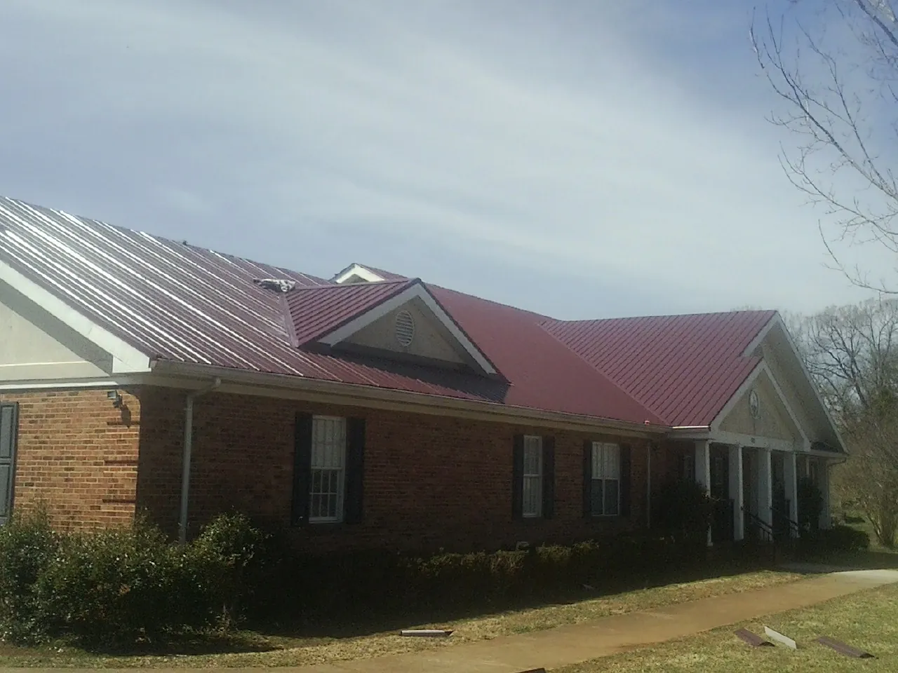 Red metal roof with gabled entries on a long brick building, from a Hail Damage Roof Repair job in Lake Dallas