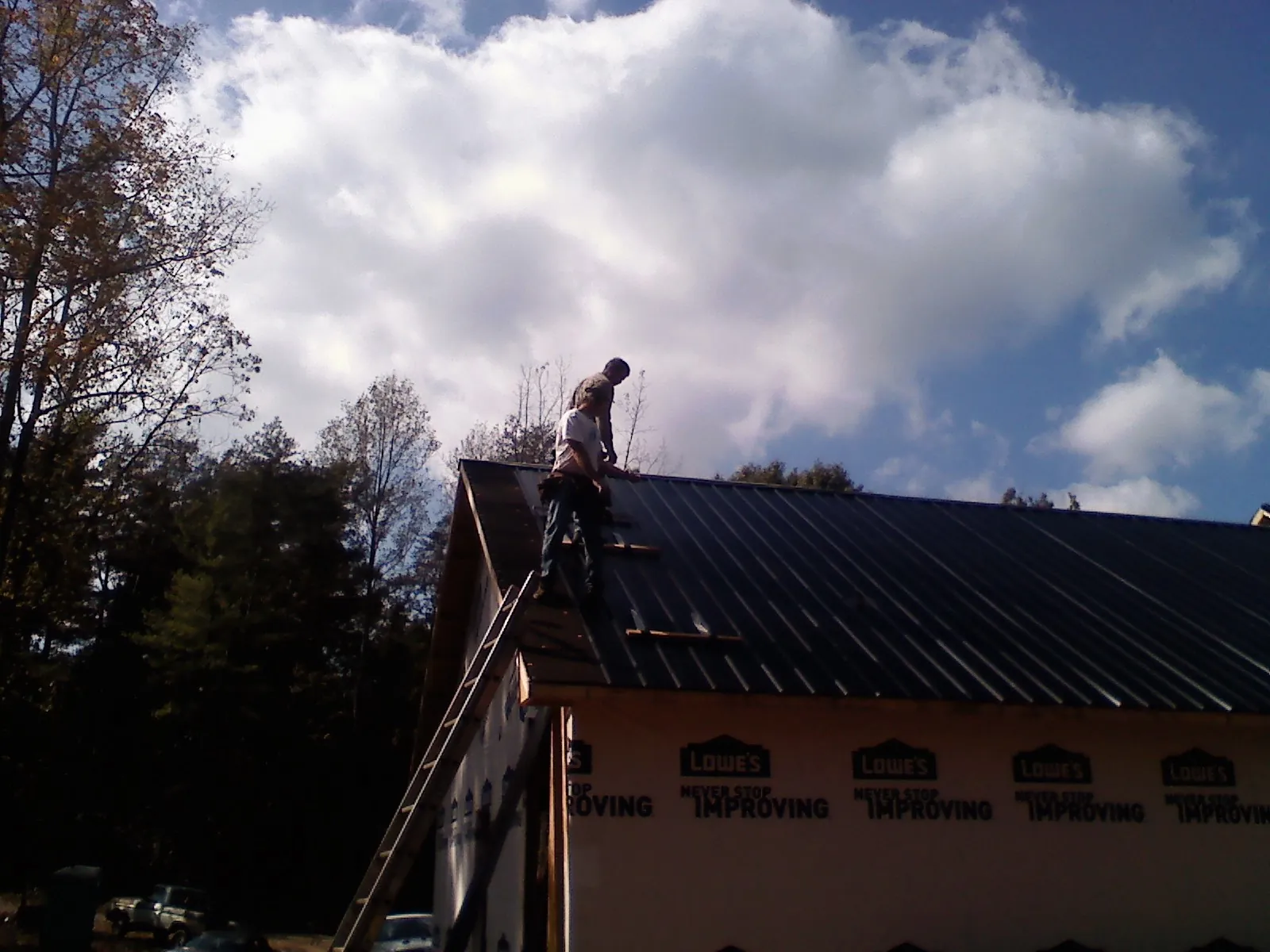 Roofer fastening dark metal panels high against a cloudy sky, from a Roof Inspection job in Lake Dallas