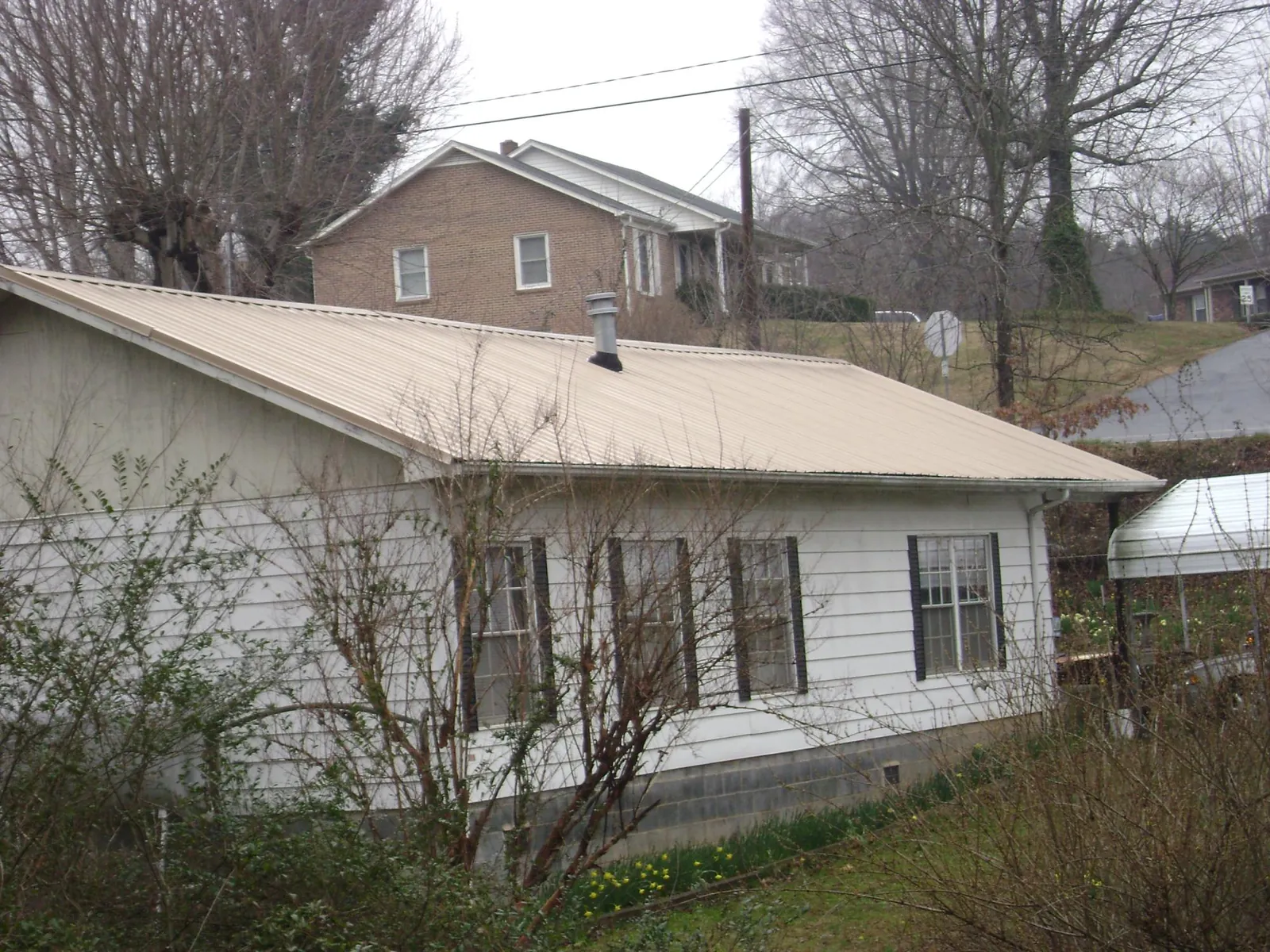 Tan metal roof on a white sided house set into a hillside — Commercial Roofing by Roofing Brothers in Lake Dallas
